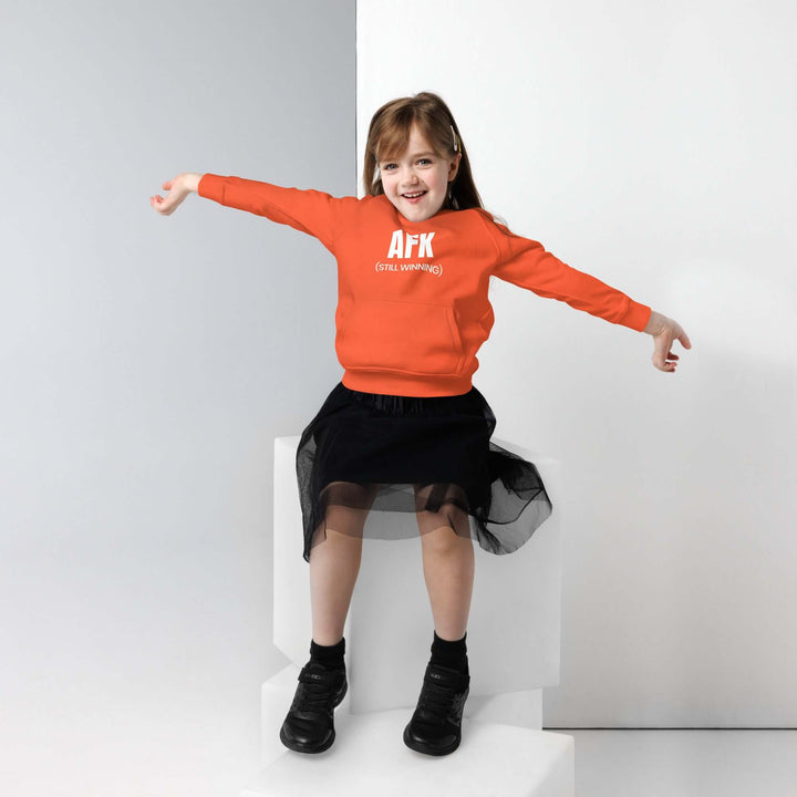 Child wearing AFK Kids eco hoodie in vibrant orange, styled with a black skirt and playful pose.